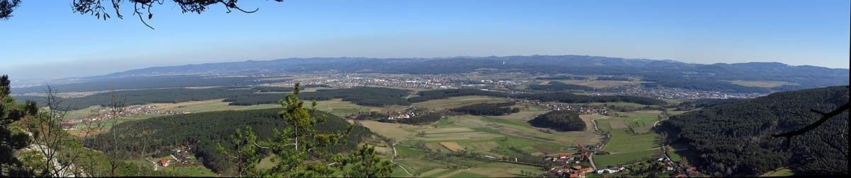 Luftaufnahme einer Landschaft mit grünen Feldern, Wäldern und einer Stadt mit vielen Gebäuden unter einem klaren blauen Himmel.