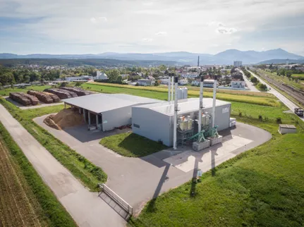 Eine Draufsicht auf eine große Industrieanlage mit mehreren Schornsteinen, umgeben von üppigen grünen Feldern und fernen Bergen.