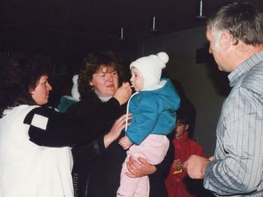 Eine Familie mit einem kleinen Kind in Winterkleidung. Die Mutter hält die Hand des Kindes, und eine andere Frau hält das Gesicht des Kindes. Ein Mann steht in der Nähe und schaut das Kind an.