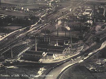 Ein schwarz-weißes Luftbild eines Industriegebiets mit mehreren Fabriken, Gebäuden und Strukturen, umgeben von Straßen und einem Fluss, datiert von Nordost Fiegeaufnahmen.