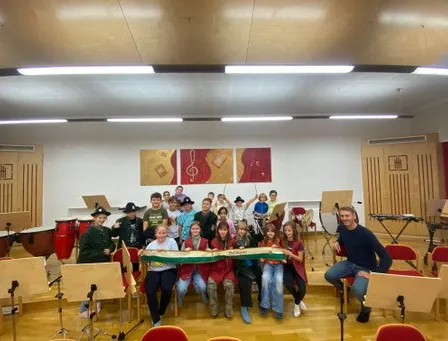 Eine Gruppe von Kindern und ein Mann posieren für ein Foto in einem Musikzimmer mit Musikinstrumenten.