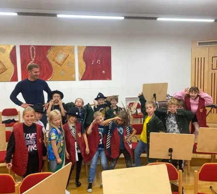 Eine Gruppe von Kindern und Erwachsenen posiert für ein Foto in einem Raum mit Musikinstrumenten und Gemälden an der Wand.