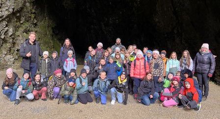 Eine Gruppe von Kindern und Erwachsenen posiert für ein Foto vor einem Höhleneingang, einige stehend, einige sitzend, alle warm gekleidet für das kalte Wetter.