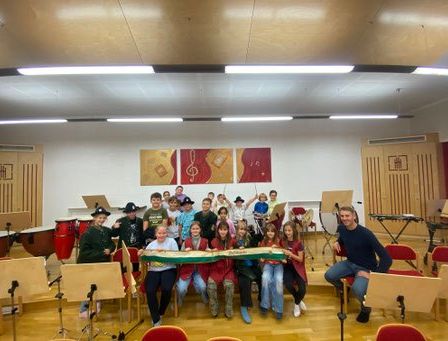 Eine Gruppe von Kindern und ein Mann posieren für ein Foto in einem Musikzimmer mit Musikinstrumenten.