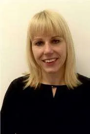 Eine Frau mit blonden Haaren, die ein schwarzes Oberteil trägt, lächelt in ein Studio in die Kamera.