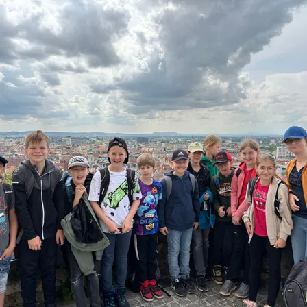 Eine Gruppe von Kindern und Jugendlichen steht lächelnd auf einem Dach und schaut in die Kamera, mit einer Stadtsilhouette im Hintergrund.