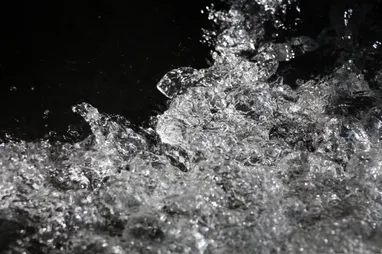 Eine Nahaufnahme von Wassertropfen, die gegen einen dunklen Hintergrund spritzen und die komplexen Details und die dynamische Bewegung des Wassers einfangen.
