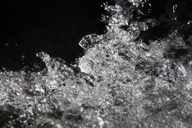 Eine Nahaufnahme von Wassertropfen, die gegen einen dunklen Hintergrund spritzen und die komplexen Details und die dynamische Bewegung des Wassers einfangen.
