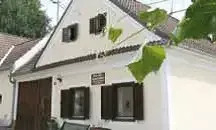 Ein weißes Haus mit braunen Begrenzungen und Fensterläden an den Fenstern, mit einer braunen Tür, einem Schild an der Wand und grünen Blättern, die vom Dach hängen.