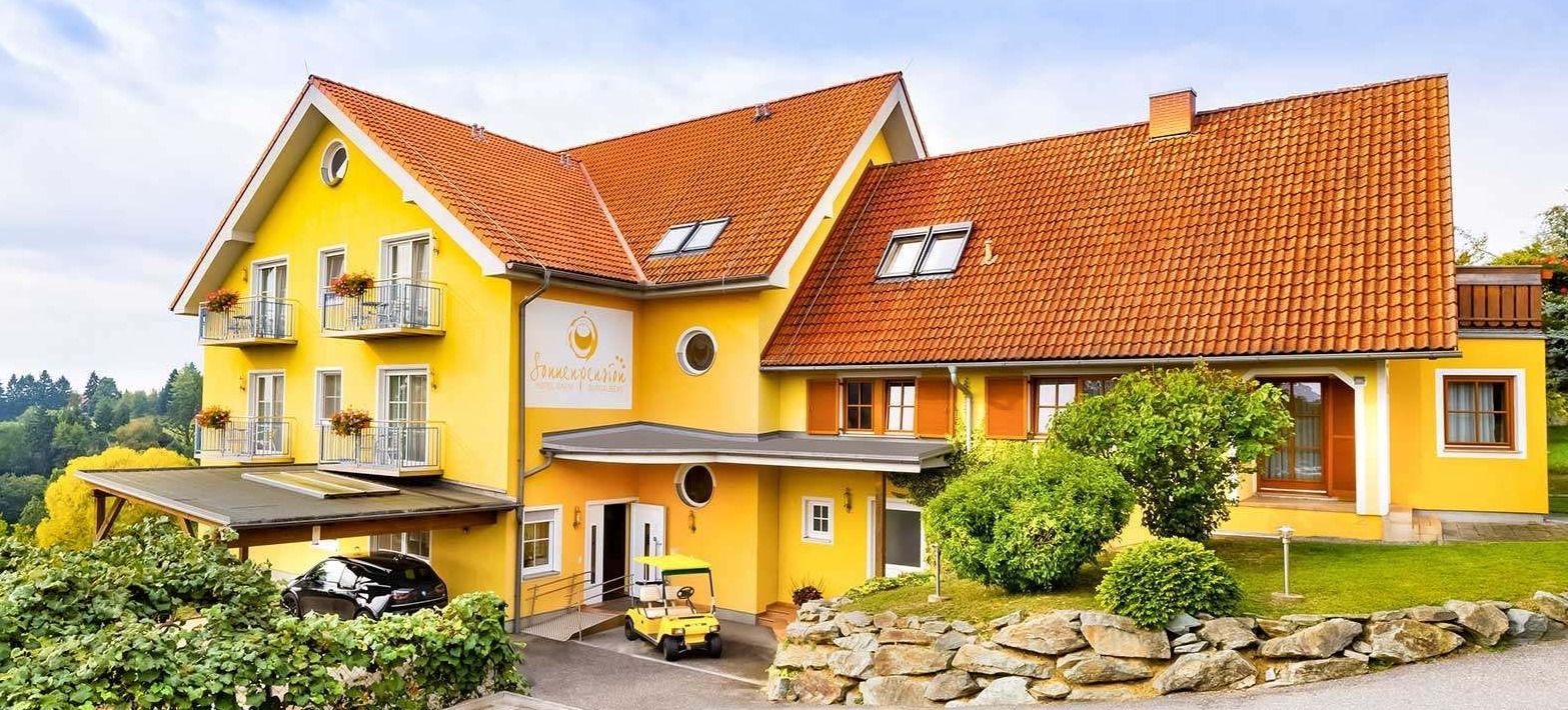 Ein leuchtend gelbes Gebäude mit rotem Dach hat mehrere Fenster und eine weiße Tür. Ein Golfwagen steht davor.
