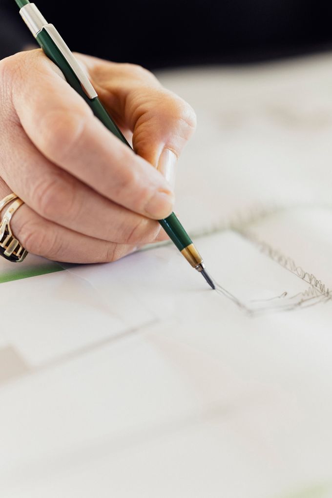  Abschnitt Bild: Nahaufnahme einer Hand, die einen Stift hält und auf einem Blatt Papier schreibt. Der Stift ist grün mit einer goldenen Spitze.