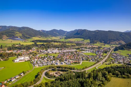 Ein Luftbild einer Stadt zwischen grünen Hügeln mit einer kurvenreichen Straße und einer Mischung aus Wohn- und Geschäftsgebäuden.