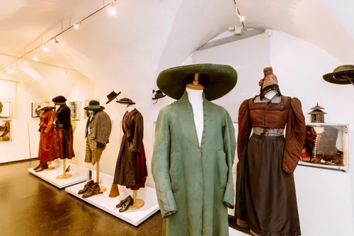 Ein Museum mit verschiedenen Vintage-Kleidungsstücken zur Ausstellung. Ein grüner langer Mantel, ein Hut und Stiefel sind auf dem zentralen Dummy. Mehrere andere Kleidungsstücke und Schuhe sind an der Seite.
