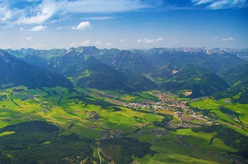 Luftaufnahme von üppigen grünen Tälern und majestätischen Bergen unter einem klaren blauen Himmel mit verstreuten Wolken.
