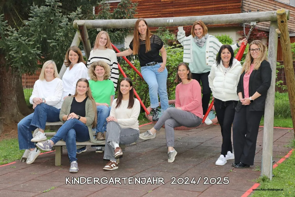 Elf Frauen posieren für ein Gruppenfoto im Spielplatz für das Kindergartenjahr 2024/2025. Sie sitzen auf Schaukeln und einer Bank.