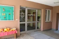 Ein Kindergarteneingang mit Glastüren und einer Aushangtafel. Ein Tisch mit Kürbissen steht vor dem Eingang.