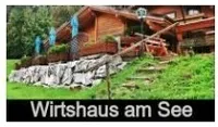 Ein Holzhaus steht auf einem Hang mit einem Grasbereich. Das Haus hat einen Zaun und eine Holzrampe. Es ist von Bäumen und Pflanzen umgeben. Der Text lautet 'Wirtshaus am See'.