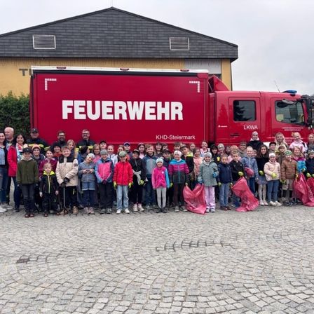 Eine Gruppe von Kindern und Erwachsenen posiert für ein Foto mit einem roten Feuerwehrauto vor einem Gebäude. Sie halten Plastiktüten.