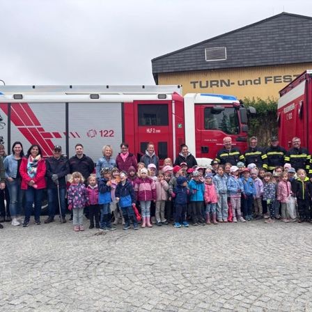 Eine Gruppe von Menschen, einschließlich Kindern, steht vor zwei roten Feuerwehrfahrzeugen mit der Nummer 122. Sie lächeln für das Foto.