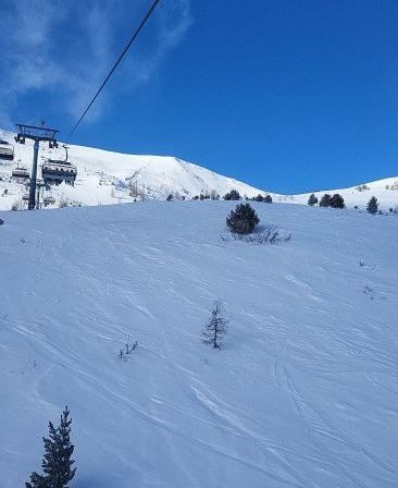 Eine Skilift auf einem verschneiten Berg unter blauem Himmel. Skispuren sind im Vordergrund sichtbar.
