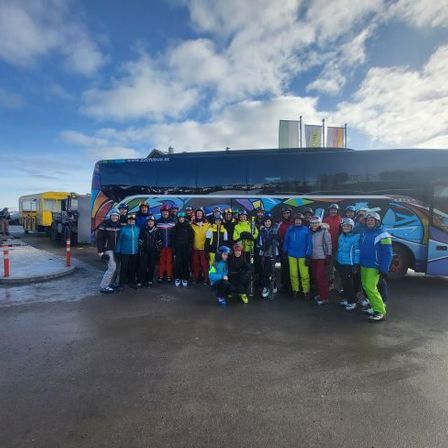 Eine Gruppe Skifahrer in bunten Ausrüstungen posiert für ein Foto vor einem großen, farbenfrohen Bus.