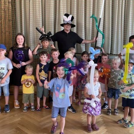 Eine Gruppe von Kindern und Erwachsenen, einschließlich eines Ballonkünstlers, posiert für ein Foto, während sie Luftballontiere und Requisiten halten.