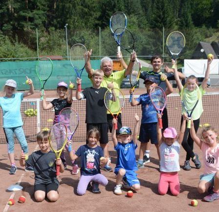 Eine Gruppe von Kindern und einem Mann posieren mit Tennisschlägern auf einem Tennisplatz. Sie alle lächeln.