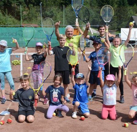 Eine Gruppe von Kindern und Erwachsenen posiert mit Tennisschlägern und Tennisbällen auf einem Tennisplatz für ein Foto.