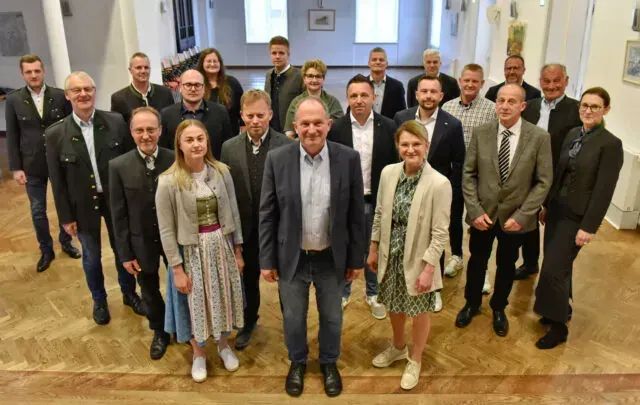 Eine Gruppe von Erwachsenen, sowohl Männer als auch Frauen, posiert für ein Foto in einem Raum. Sie sind alle formell gekleidet.