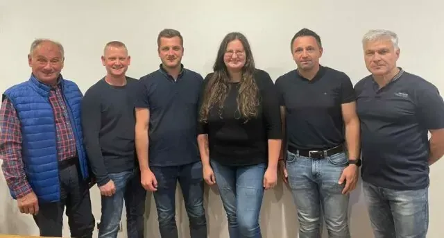 Sechs Personen, drei Männer und drei Frauen, stehen zusammen für ein Gruppenfoto. Sie tragen alle Freizeitkleidung, und die Frau in der Mitte lächelt.