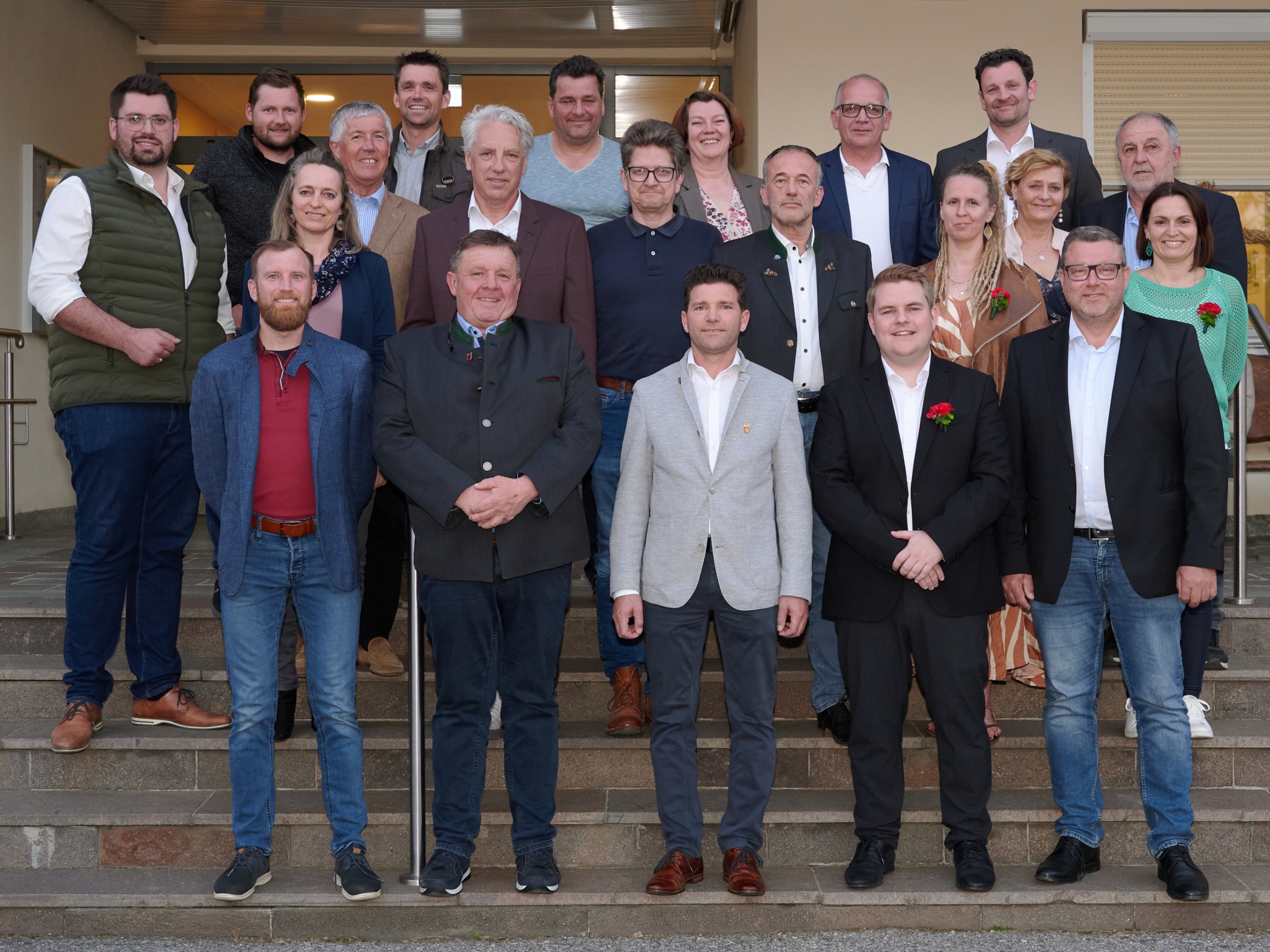 Eine Gruppe von Menschen in formeller und lässiger Kleidung, die auf einer Treppe mit einem Hintergrund eines Gebäudes stehen.