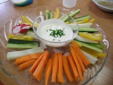 Ein Glasteller mit einer Vielzahl bunter Gemüse, die in einem Kreis angeordnet sind, zusammen mit einer Schüssel Dip.