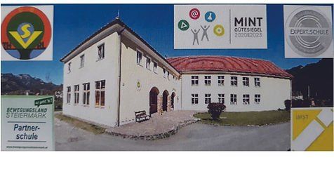 Ein weißes Gebäude mit rotem Dach und mehreren Fenstern, beschriftet mit 'Partner-schule' und 'MINT Guter Siegel 2020/2023'. Es gibt Logos und Schilder rund um das Gebäude.