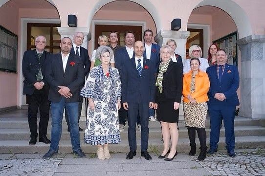 Eine Gruppe von Menschen in formeller Kleidung und Schuhen posiert für ein Foto vor einem rosa Gebäude.