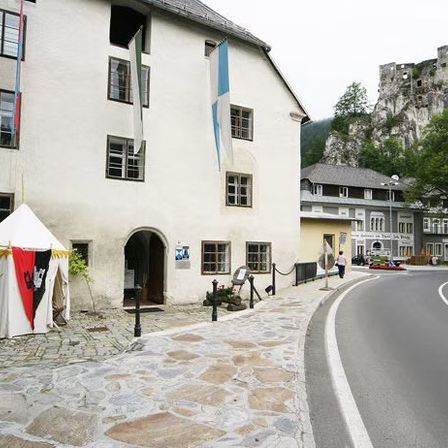 Eine Straße mit Gebäuden gesäumt, eines mit einer Flagge, neben einer Burg auf einem Felsen unter einem klaren Himmel.