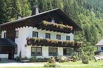 Ein großes weißes und braunes Chalet mit mehreren Balkonen und Schornsteinen, umgeben von Grün und Bergen.