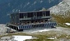 Ein großes Gebäude mit Solarpanelen, auf einem schneebedeckten Berghang gelegen, umgeben von einem grünen Grasfeld.