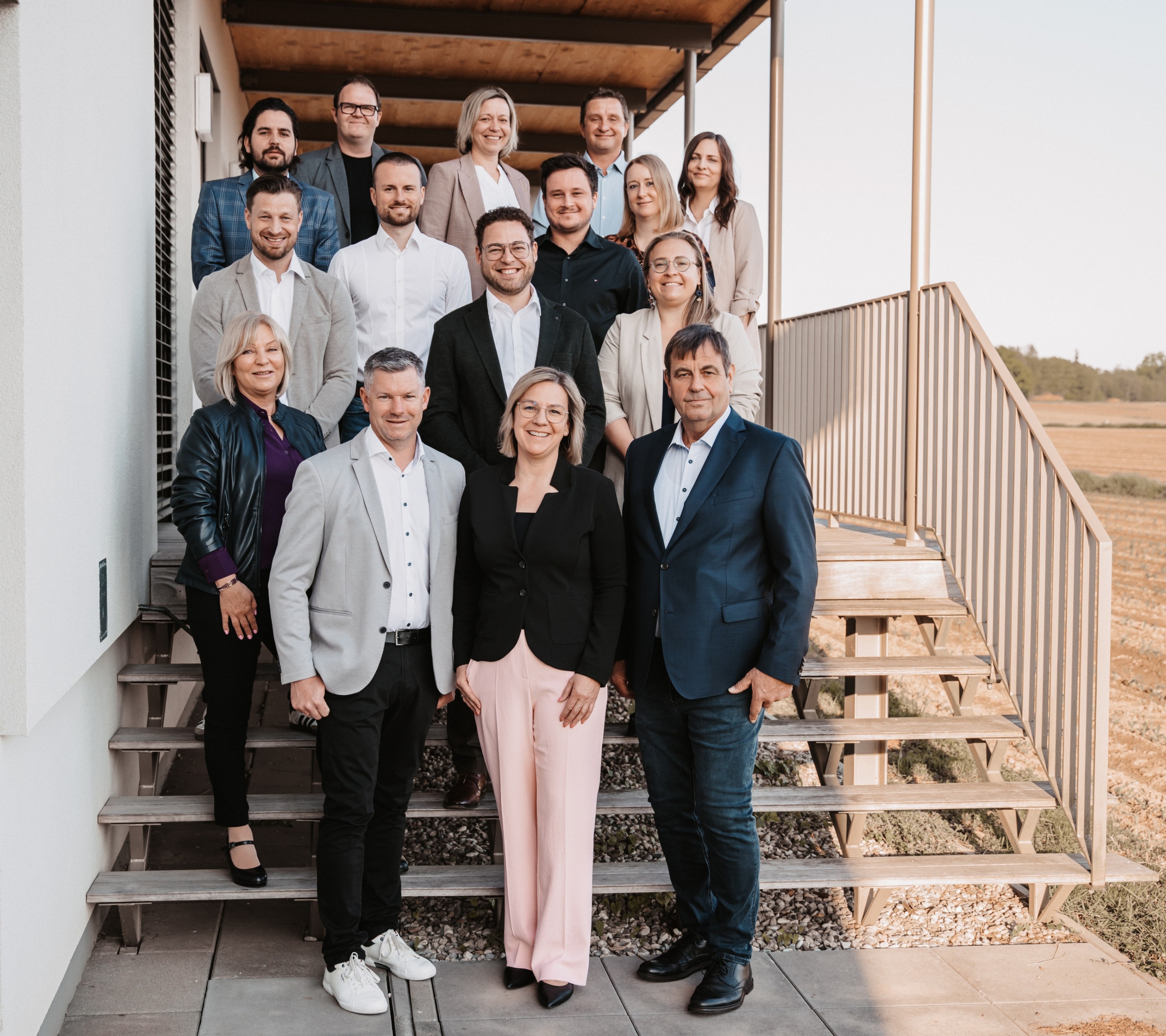 Eine Gruppe von Fachleuten steht auf den Stufen eines modernen Gebäudes und lächelt für ein Teamfoto.