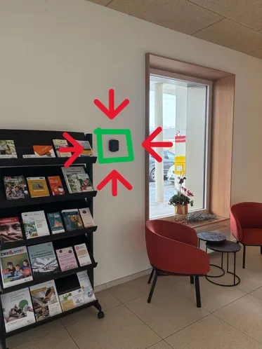 Ein Raum mit einem Bücherregal voller Bücher, zwei roten Stühlen und einem kleinen Tisch. Es gibt ein grünes Quadrat und rote Pfeile an der Wand.