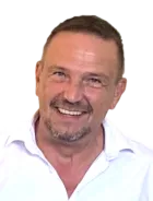 Ein Mann mit kurzem Haarschnitt und weißem Polohemd lächelt breit und zeigt Zähne vor schwarzem Hintergrund.