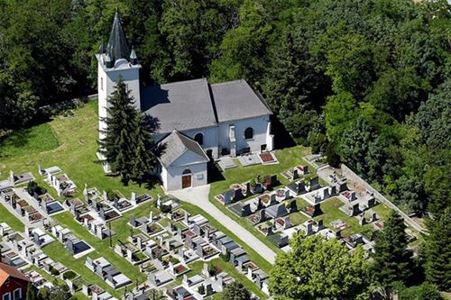 Eine Luftaufnahme einer Kirche, umgeben von einem Friedhof mit vielen Grabsteinen und Bäumen.