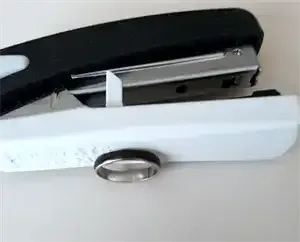 Ein schwarz-weißer Hefter mit Metallrahmen und schwarzem oberen Teil wird auf einer weißen Oberfläche gezeigt. Es ist ein Metallring am unteren Teil befestigt.