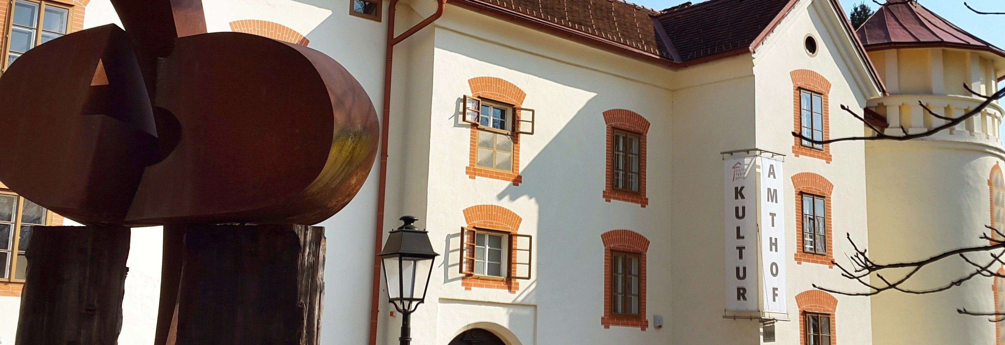 Ein weißes Gebäude mit Ziegelfensterrahmen, braunem Dach und einer Laterne. Zwei Fenster sind offen und werfen Schatten.