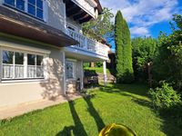 Ein Haus mit Balkon und Garten mit Tisch und Stühlen. Das Haus hat ein braunes Dach und weiße Wände.