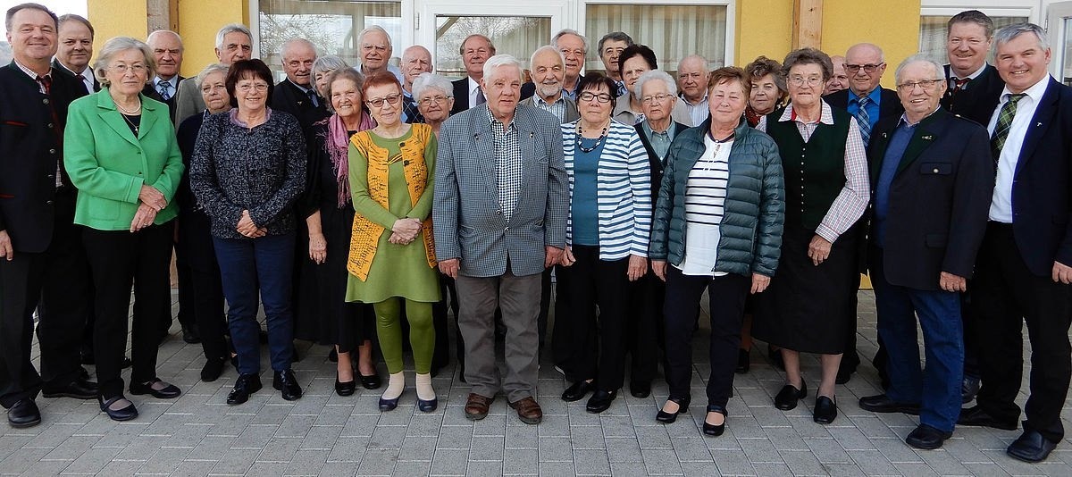 Eine Gruppe älterer Menschen, darunter Männer und Frauen, posiert für ein Foto vor einem Gebäude.