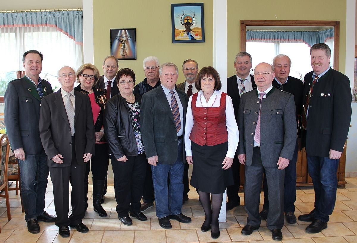 Eine Gruppe formell gekleideter Personen, sowohl Männer als auch Frauen, stehen für ein Foto in einem Raum mit hellgelben Wänden und Gemälden.