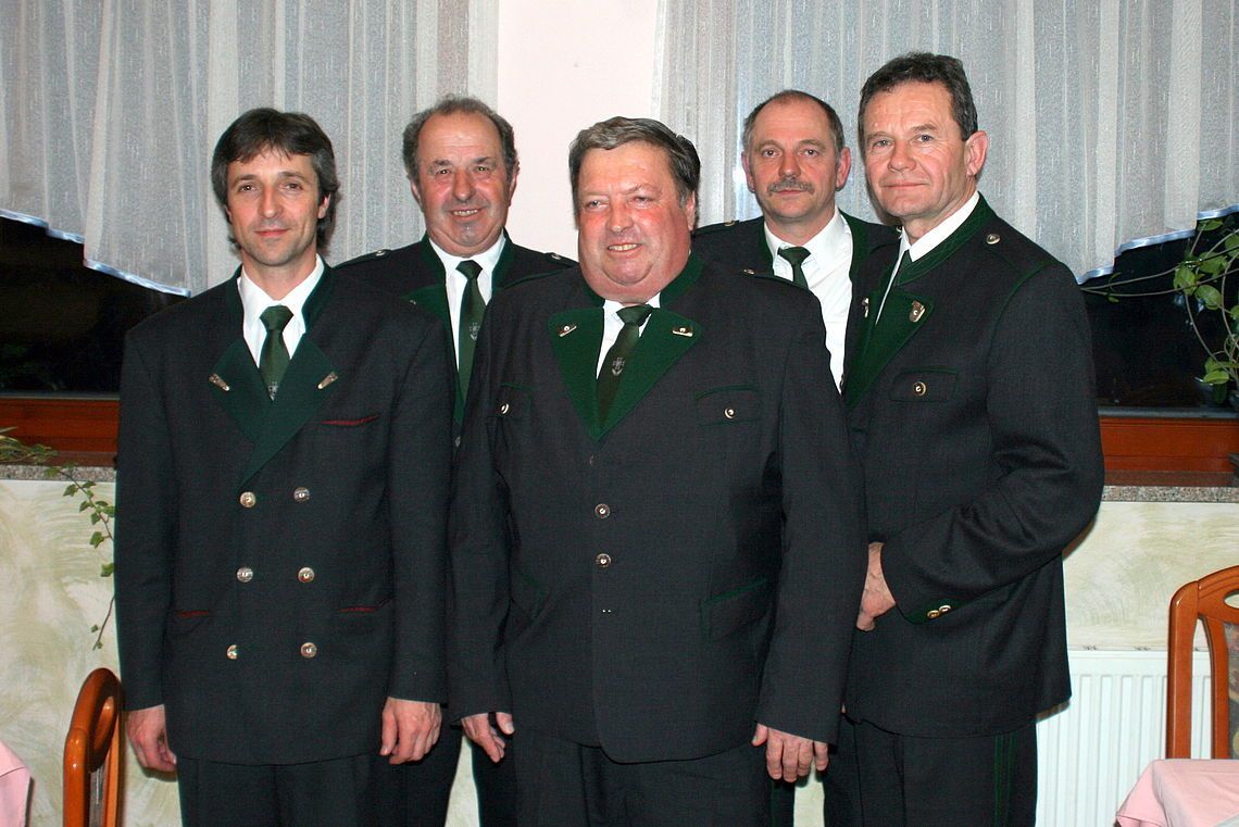 Fünf Männer in übereinstimmenden Uniformen posieren für ein Foto. Sie tragen schwarze Anzüge mit grünen Krawatten und weißen Hemden. Der Mann in der Mitte lächelt und hat leicht geöffneten Mund.