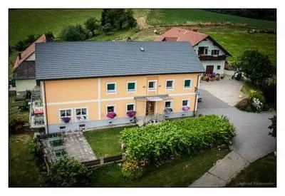 Ein Luftbild eines gelben Hauses mit grauem Dach, umgeben von üppigem Grün, einer Auffahrt und einem Nachbarhaus mit rotem Dach.