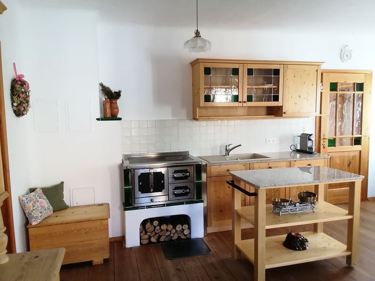 Eine gemütliche Küche mit Holzschränken, einer gefliesten Rückwand, einer hängenden Lampe, einer Kaffeemaschine, einem Herd und einem Holztisch mit Granitplatte.