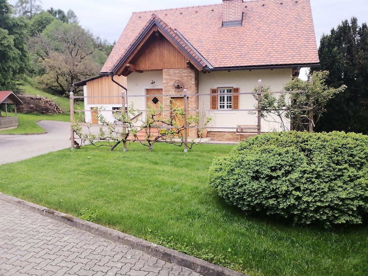 Ein modernes Haus mit rotem Ziegeldach und Ziegelwänden, umgeben von einem Zaun und einem gepflegten Garten mit einem Busch und einer Bank.
